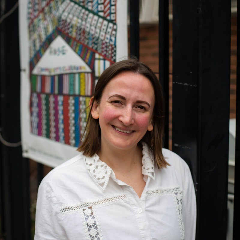 Megan Barrett, a white woman with shoulder length brown hair smiles brightly at the camera wearing a white top