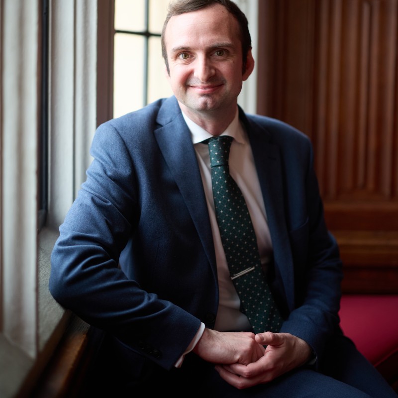Owen Day, a white man wearing a suit smiles at the camera
